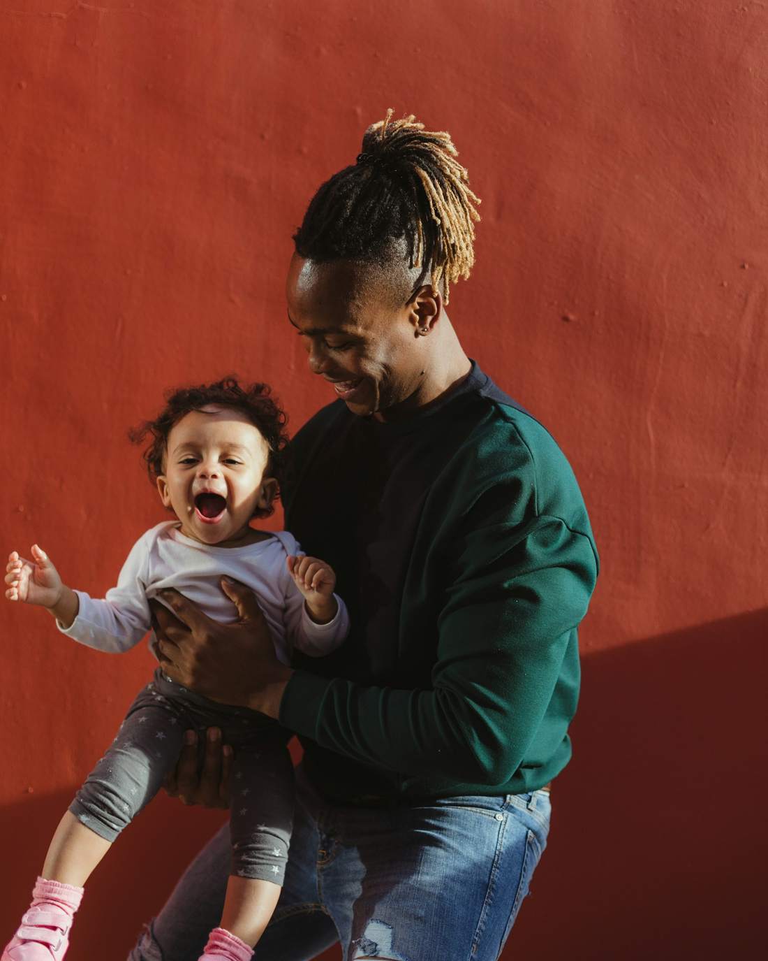 A father laughing as he lifts his toddler